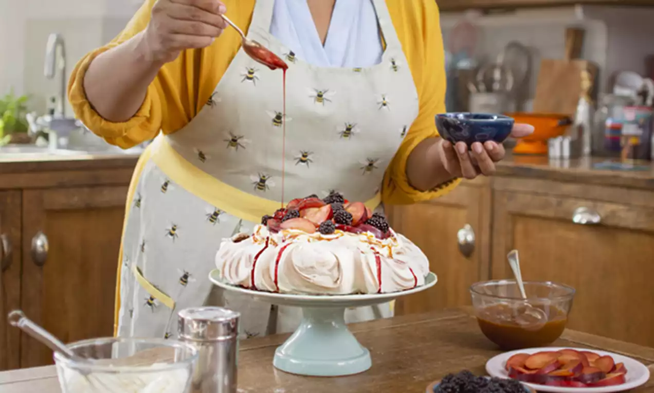 White meringue base topped with glossy blackberries, sliced strawberries, and caramel drizzle on a pale blue pedestal plate