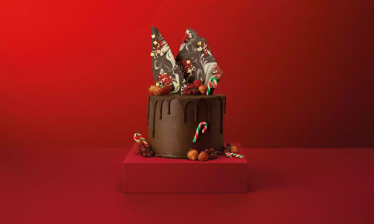 Dark chocolate cake with smooth ganache drip, topped with marbled chocolate shards, red candy canes, strawberries and gold-dusted sprinkles