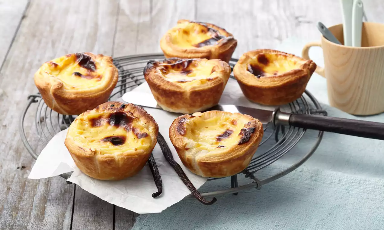 Petits flans dorés avec une surface légèrement caramélisée, dans des croûtes croustillantes disposés sur une grille avec des bâtons de vanille