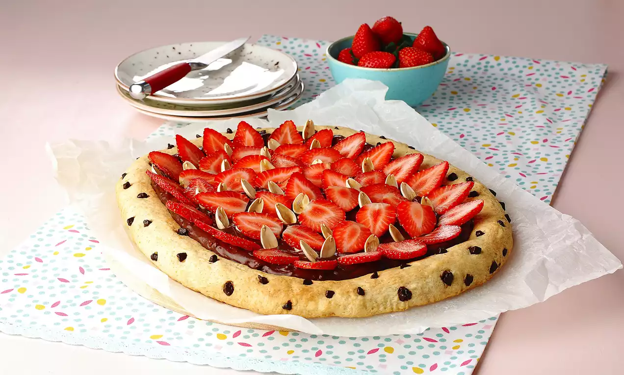 Çikolata parçacıklı hamur üzerinde çikolata kreması, taze dilimlenmiş çilekler ve kabak çekirdekleriyle süslenmiş tatlı pizza