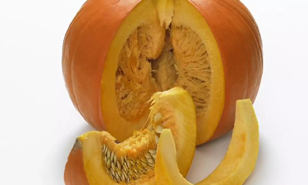 Citrouille ronde orange vif avec une tige verte, coupée en quartiers dévoilant sa chair jaune et ses graines sur une surface blanche