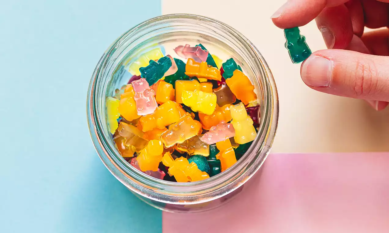 Barevní gumoví medvídci bez želatiny s průsvitnou texturou v odstínech oranžové, žluté, růžové, zelené a čiré v malé skleněné misce na pastelovém pozadí