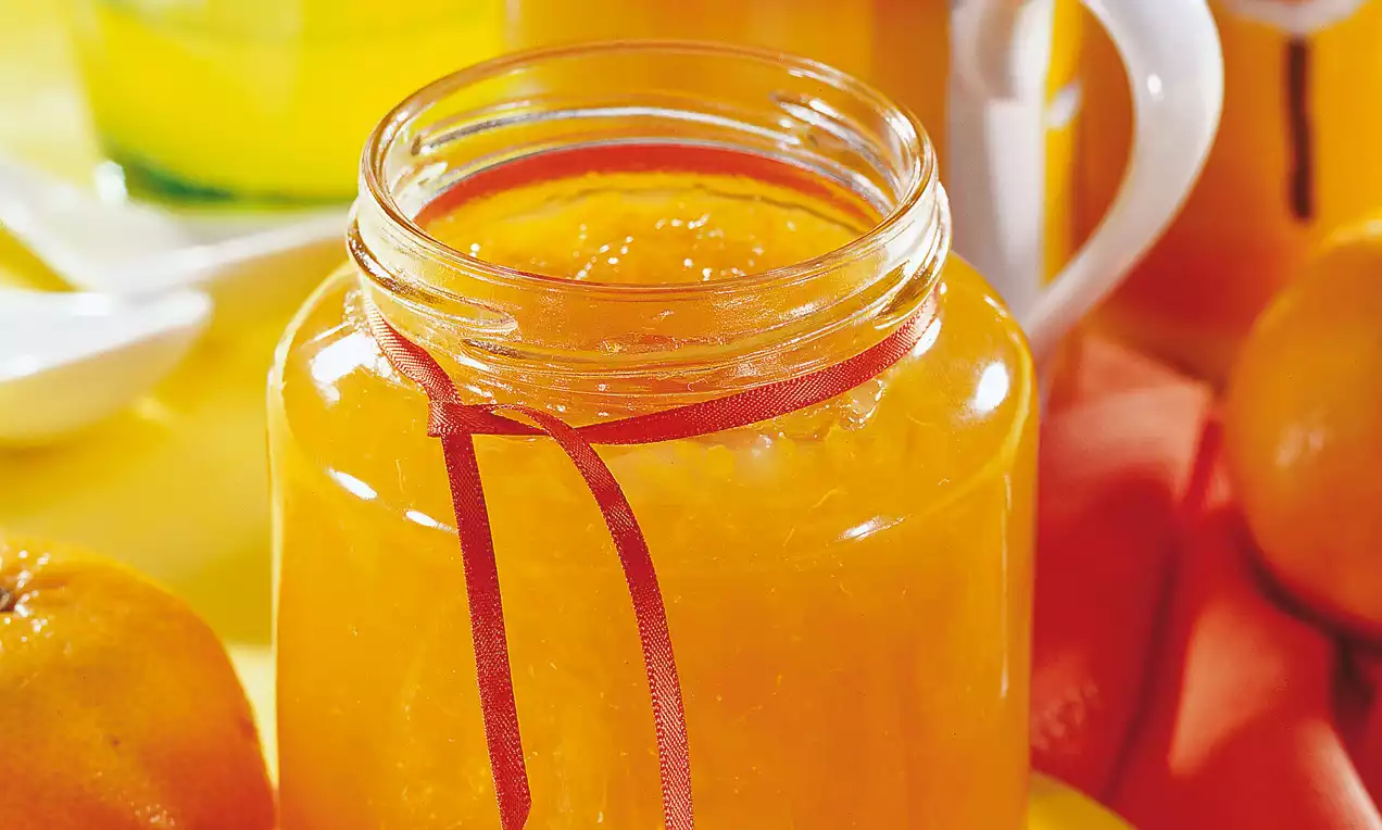 Confettura di mandarini arancione brillante in un barattolo di vetro decorato con nastro rosso, circondato da mandarini e dettagli giallo vivo