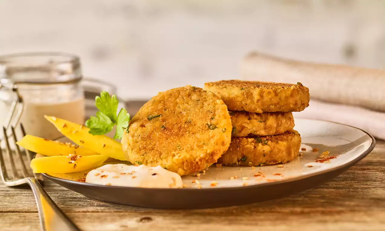 Goldbraune Gemüsebratlinge mit knuspriger Oberfläche, angerichtet auf einem Teller mit Mango-Streifen, cremigem Dip und Petersilie