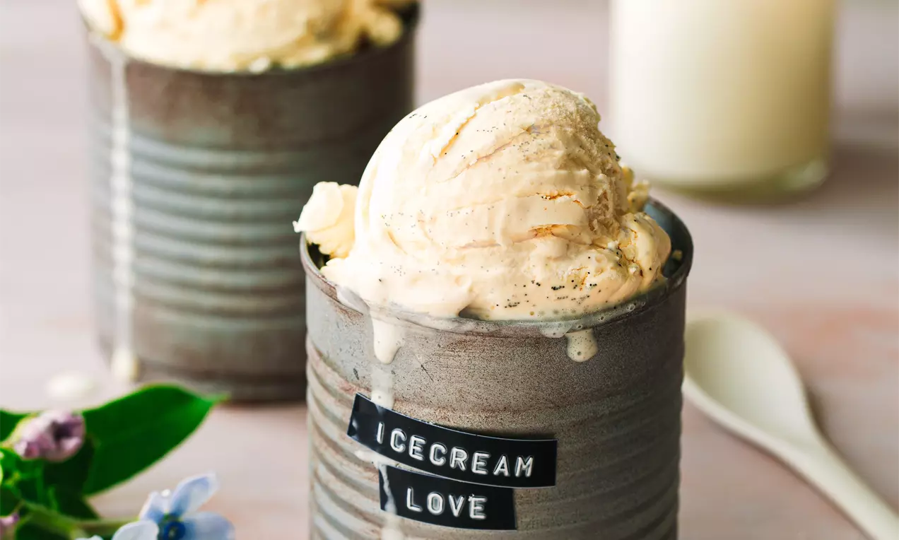 Picture - Scoops of pale beige vanilla ice cream with a smooth texture served in rustic grey tins, garnished with flowers and a spoon nearby