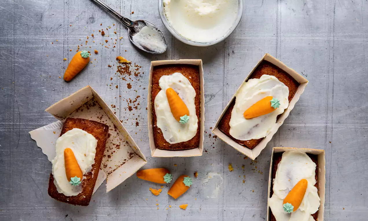 Minicakes rectangles dorés à la carotte garnis de crème blanche lisse et décorés de petites carottes en pâte d’amande orange