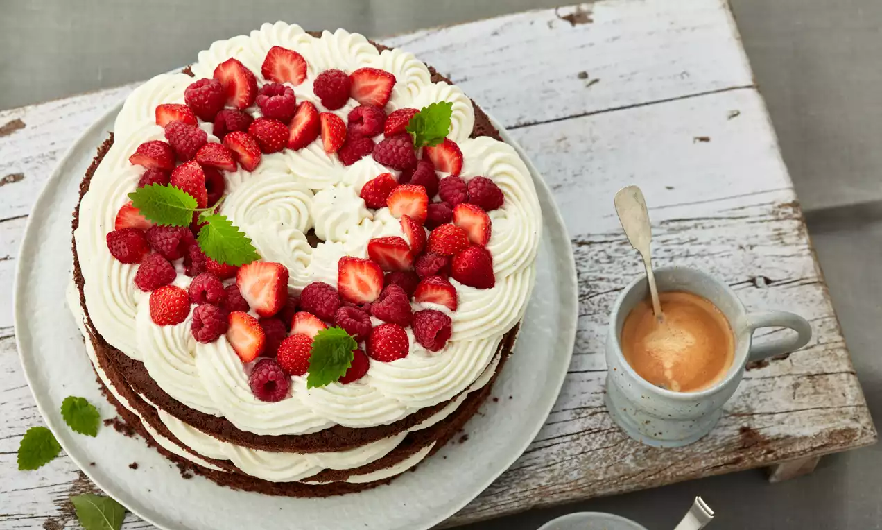 Plasti čokoladnega biskvita z gladko mascarpone kremo, okronane z jagodami, malinami in listi mete na rustikalnem krožniku