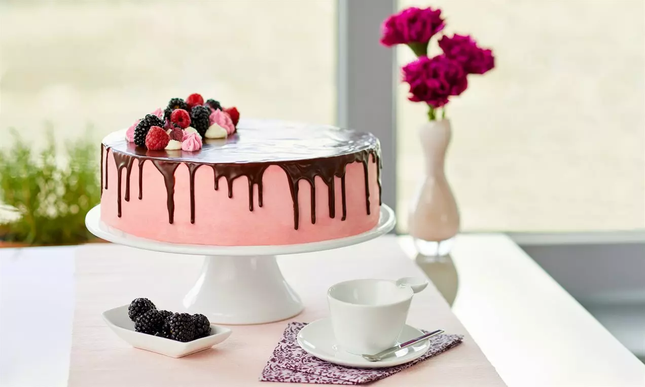 Розова торта с гланцирана шоколадова глазура и течащи капки, украсена с малини, боровинки и целувки върху бяла поставка