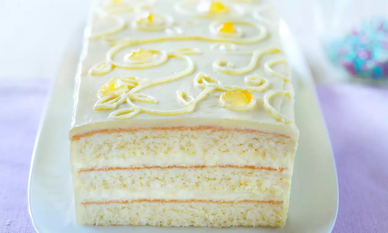 Prostokątne ciasto o jasnokremowych warstwach biszkoptu i ajerkoniakowego kremu, ozdobione żółtymi wzorami na białym półmisku
