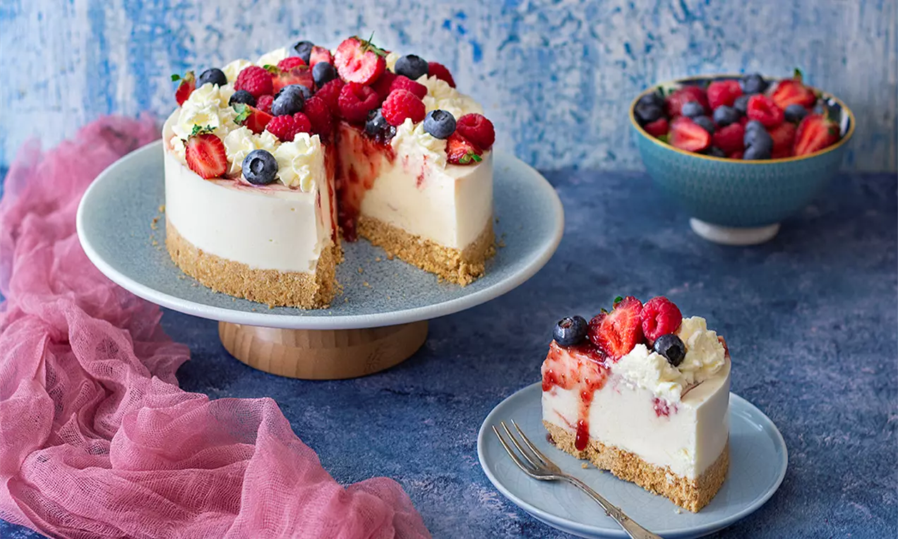Кремообразен сладоледен чийзкейк върху хрупкав бисквитен блат, гарниран с малини, ягоди, боровинки, бита сметана и ягодов сироп