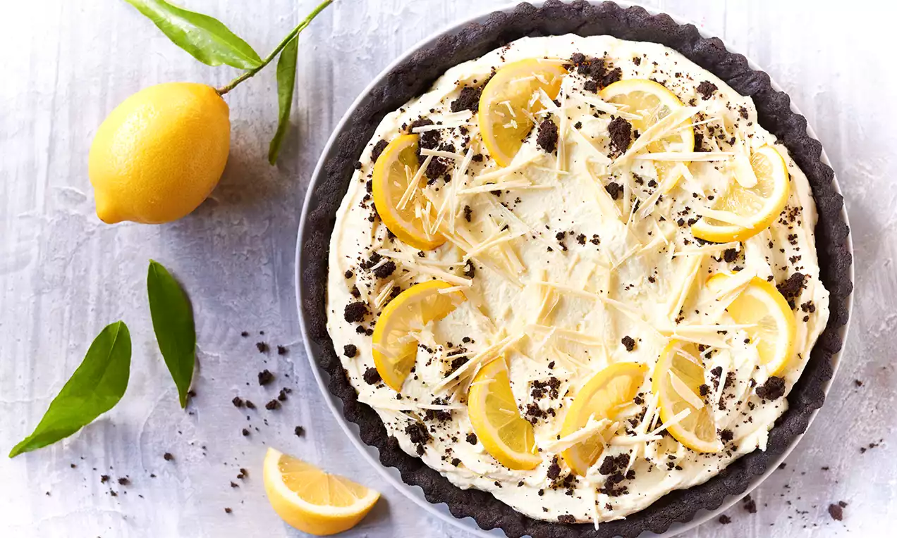 Tarta cytrynowa na ciemnym kruchym spodzie, z kremowym nadzieniem, plasterkami cytryn, wiórkami białej czekolady i kruszonką