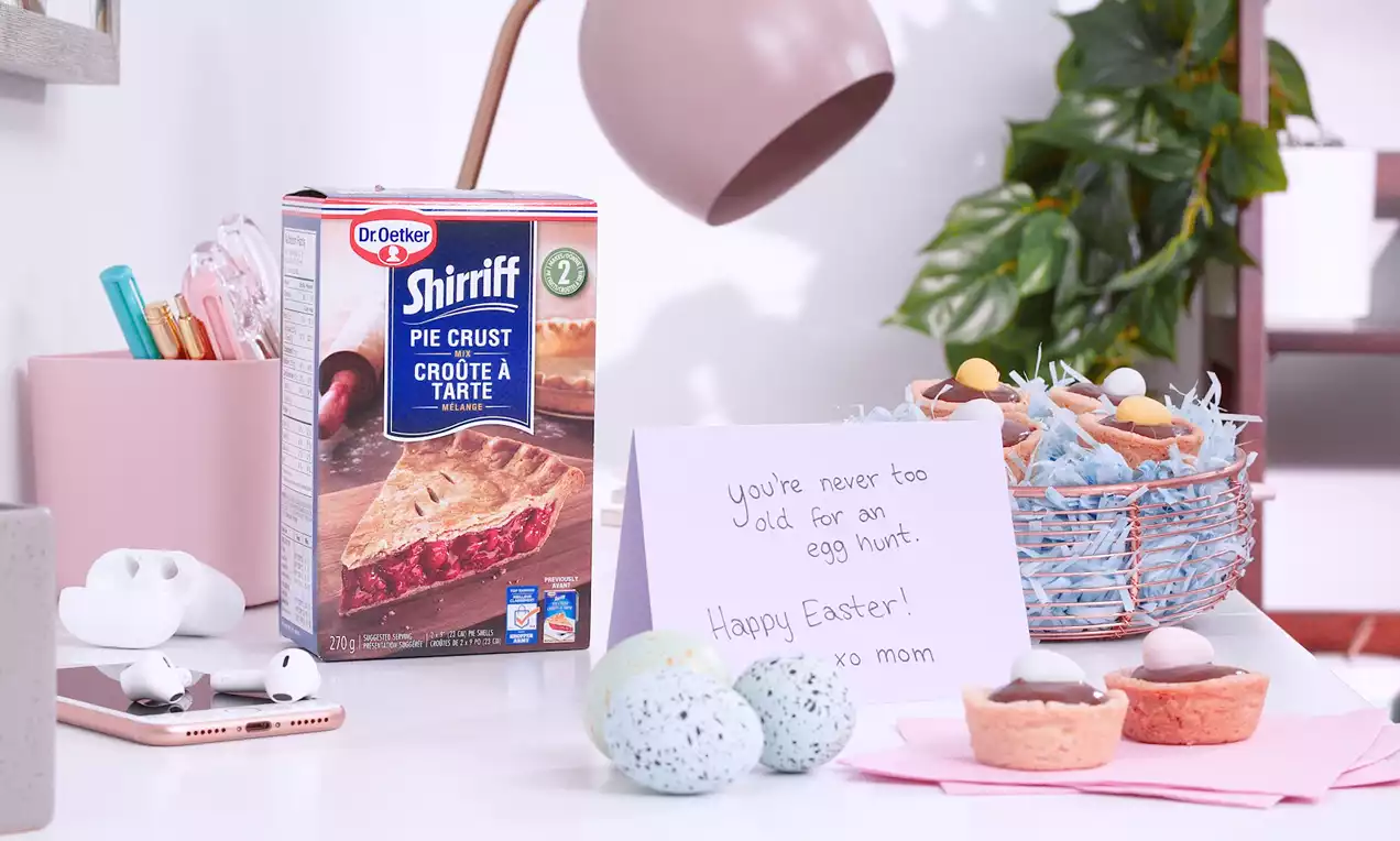 Easter basket pudding cups with smooth chocolate filling, colorful candy eggs, and shredded blue paper in a pastel blue wire basket