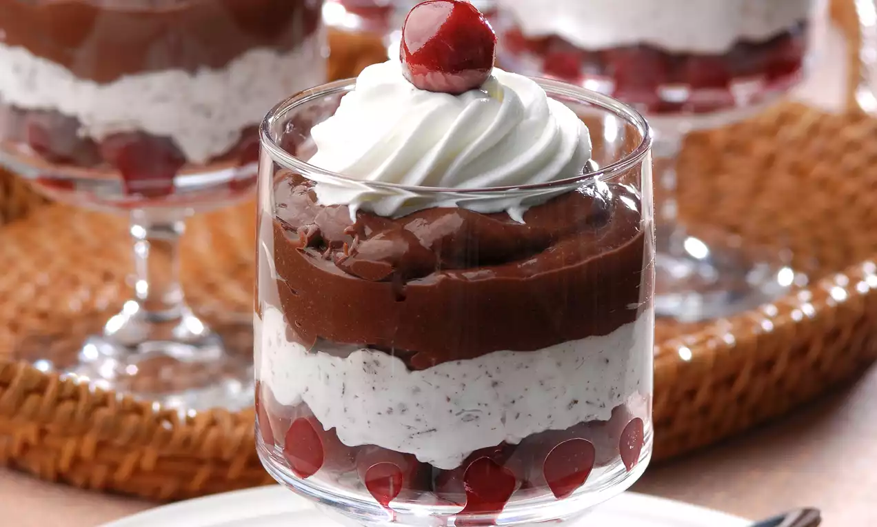 Cam bardakta katmanlı olarak dizilmiş çikolata kreması, beyaz vanilyalı köpük, vişneler ve üstünde krem şanti ile süslenmiş