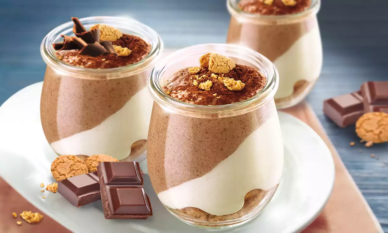 Zweifarbiges Dessert in Gläsern mit brauner Mousse und weißer Creme, dekoriert mit Keksstücken und Schokoraspeln auf weißem Teller