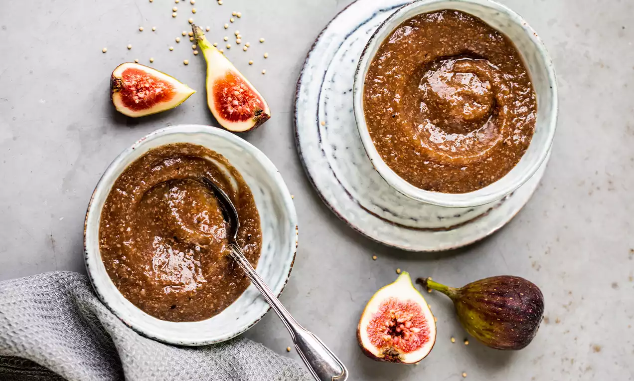 Moutarde brune épaissie et granuleuse dans des bols en céramique blanche, entourée de figues fraîches coupées et un torchon gris