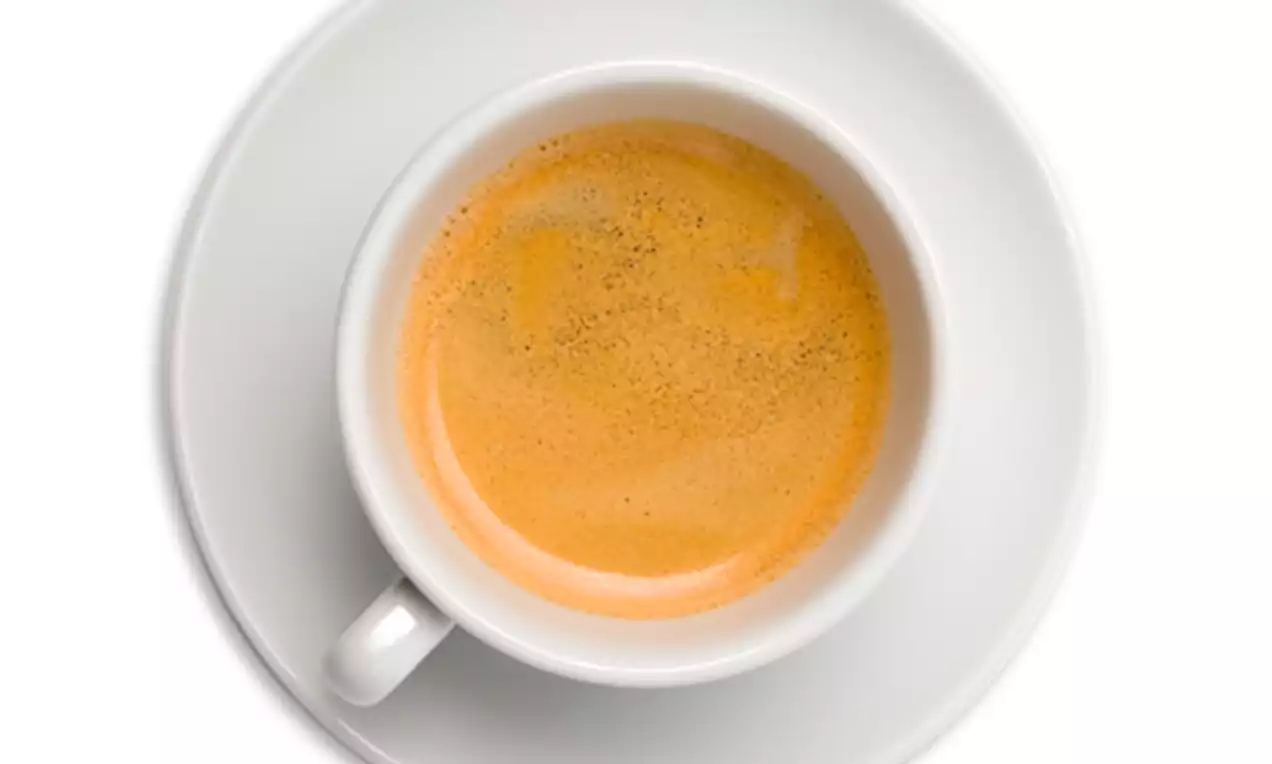 Witte koffiekop gevuld met romige, goudbruine espresso met een dunne schuimlaag, geplaatst op een bijpassend wit schoteltje