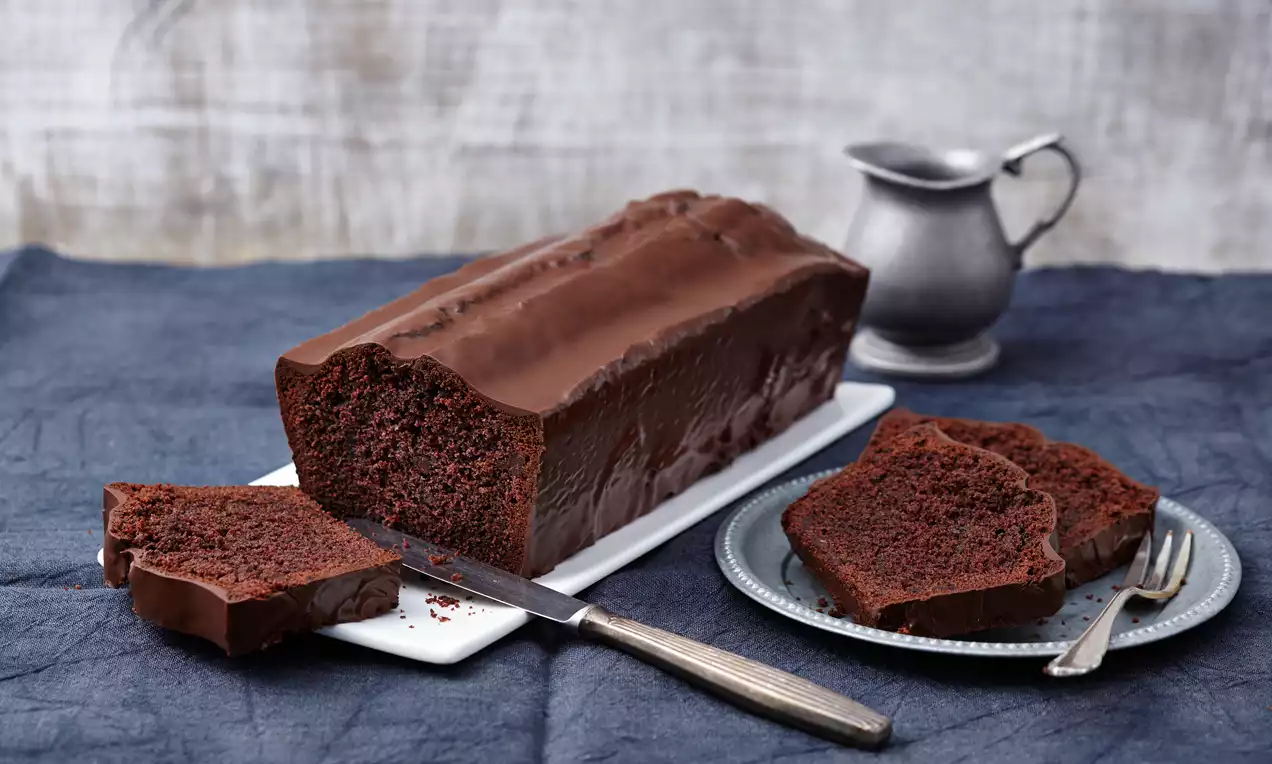 Yoğun çikolatalı baton kek dilimleri, pürüzsüz çikolata kaplamasıyla birlikte metal bir bıçak ve tabağa yerleştirilmiş