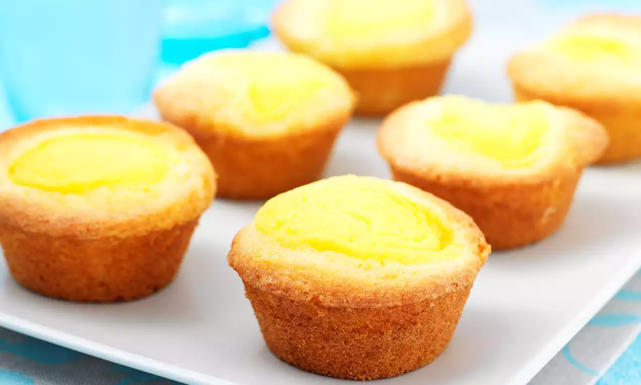 Goudbruine puddingcakejes met gladde lichtgele vulling, gerangschikt op een wit bord met blauwe decoratieve achtergrond