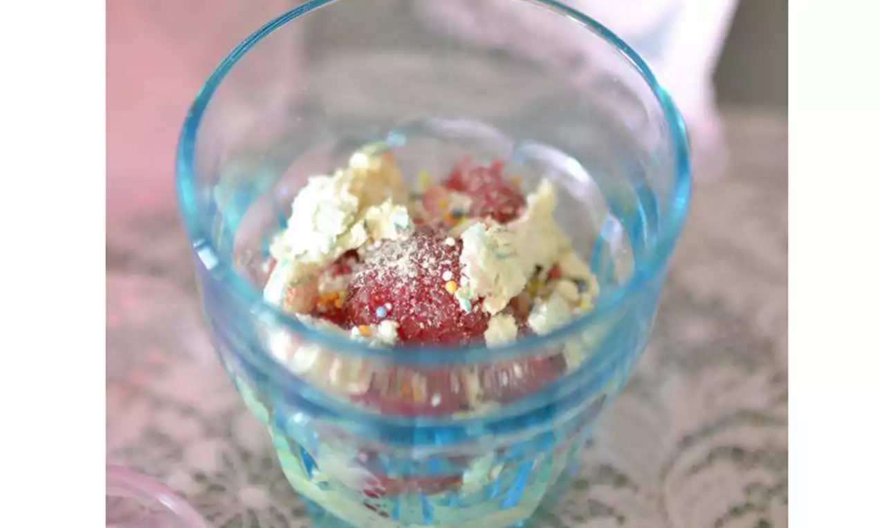 Dessert trifle dans une coupe bleue translucide avec des couches de crème pâle et morceaux de fruits rouges sous une lumière douce