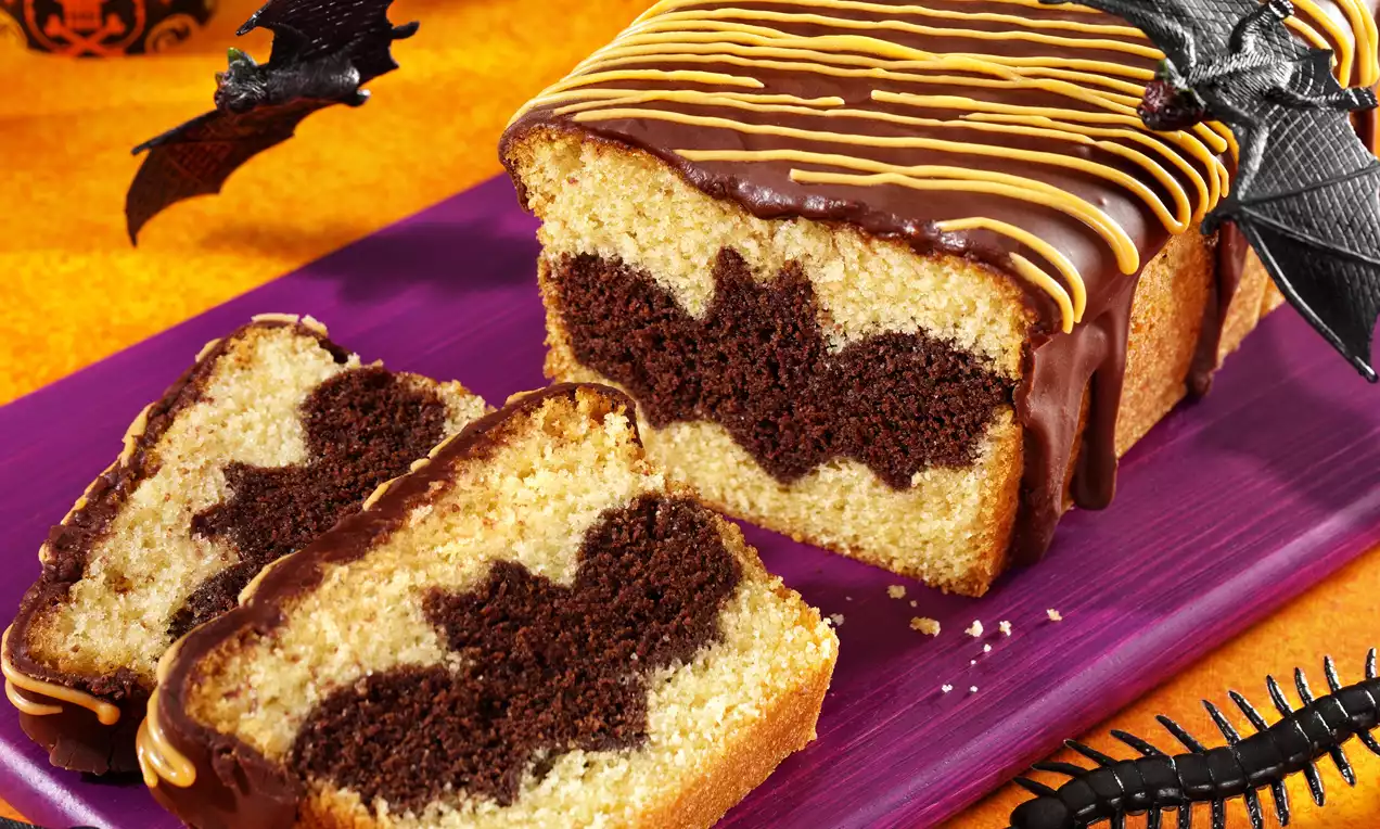 Cake marbré beige et chocolat avec des motifs intérieurs en forme de chauve-souris, glaçage chocolat brillant et décorations orange dessus