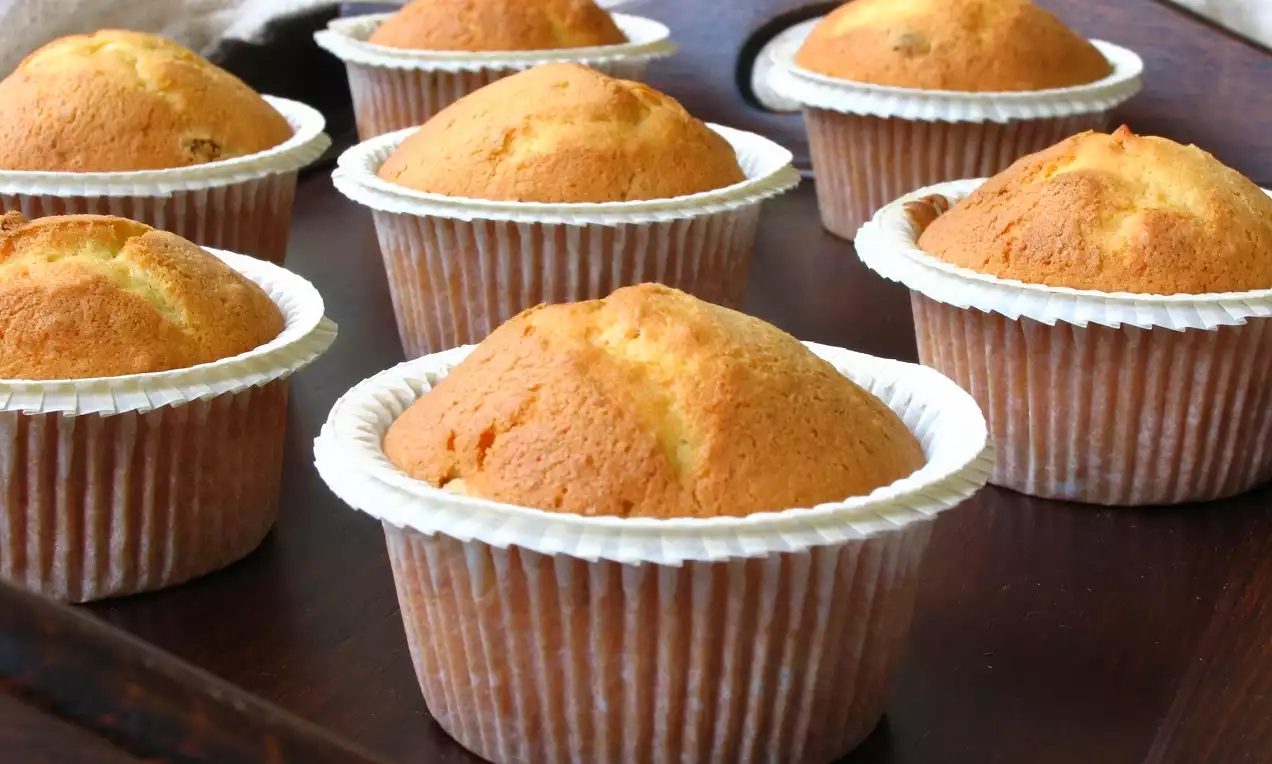 Altın rengi yumuşak dokulu üzüm ve fındıklı muffinler, beyaz kağıt kalıplarda ahşap bir tepsi üzerinde düzenli bir şekilde sıralanmış