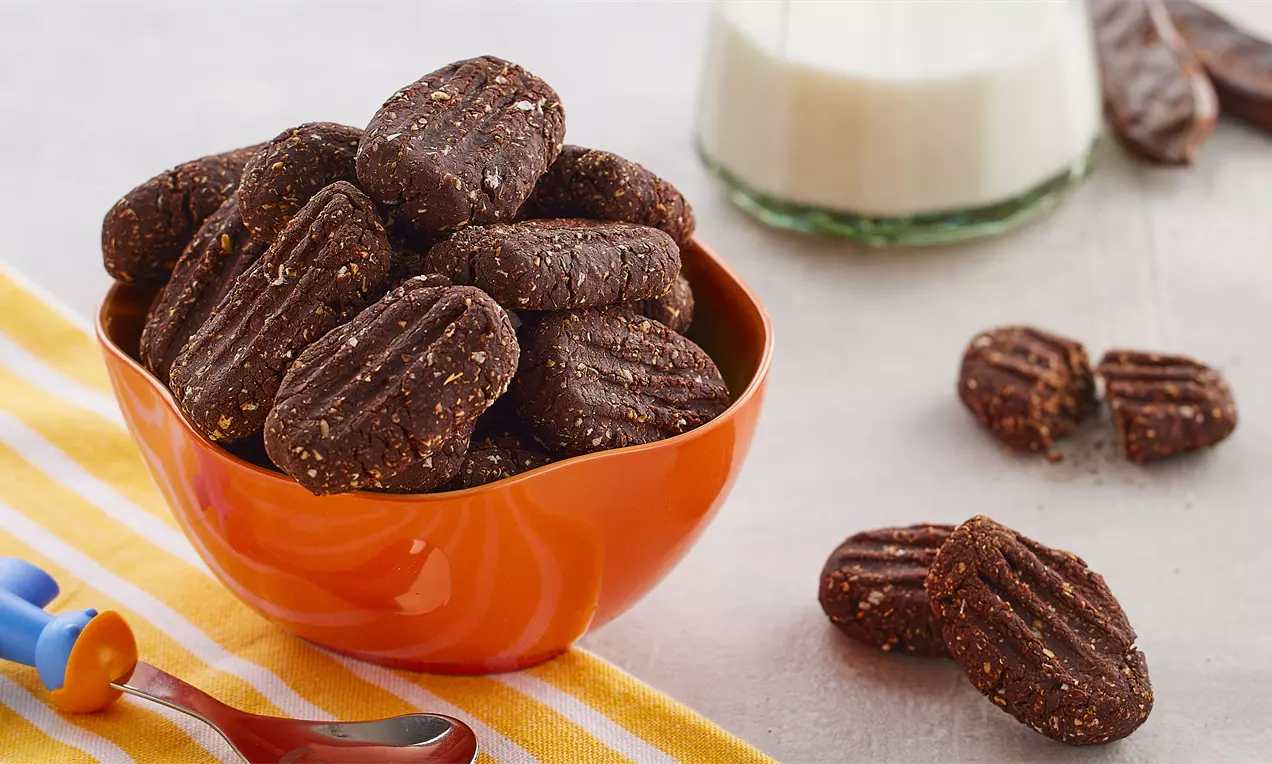 Portakal renkli bir kaseye dolu şekilde yerleştirilmiş, kahverengi ve kıvrımlı yüzeye sahip keçiboynuzlu bisküviler yulaf taneleri içeriyor