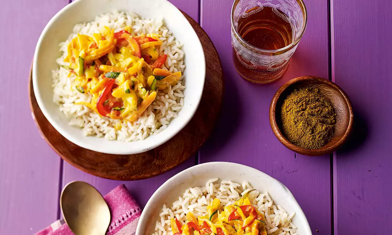 Bunte indische Gemüsecurry-Sauce mit gelblicher, cremiger Textur, verteilt über weißem Reis in zwei Schalen auf lilafarbenem Tisch