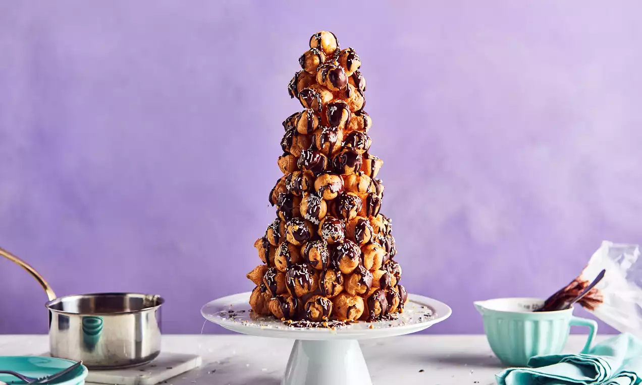 Towering croquembouche of golden choux buns glazed with chocolate and orange, arranged in a cone on a white pedestal plate