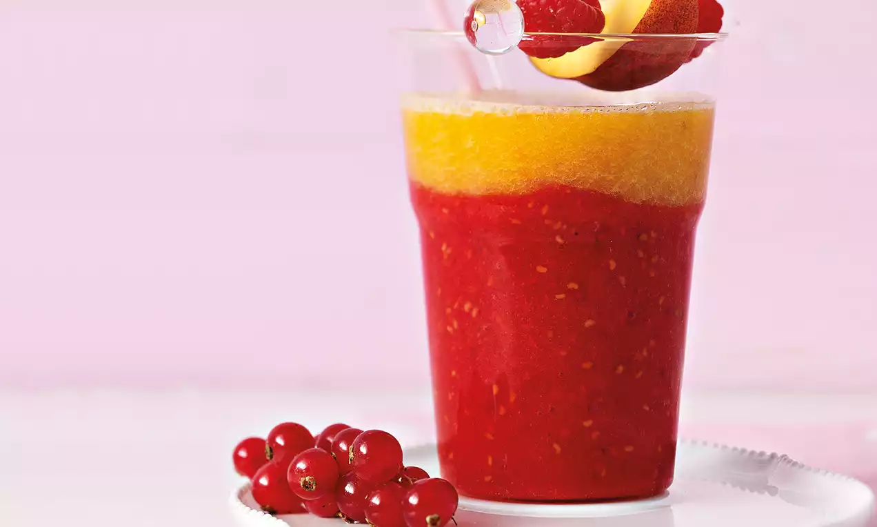Smoothie rouge intense et jaune vif avec framboises, groseilles et pêche en garniture sur une assiette blanche