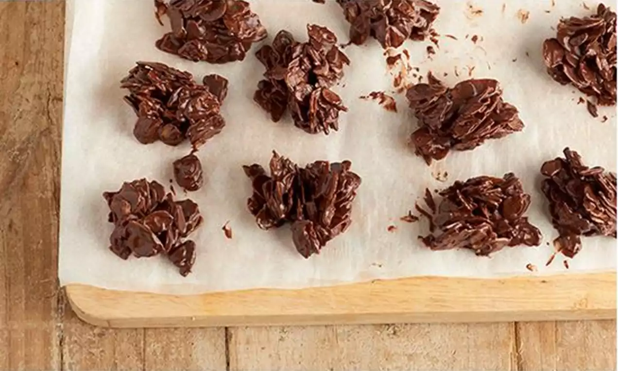 Montoncitos irregulares de láminas de almendra cubiertas de chocolate oscuro brillante sobre papel blanco sobre una tabla de madera clara