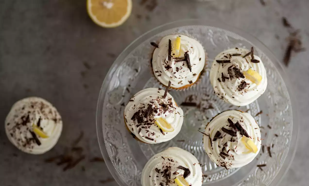 Maigi brūni šokolādes keksiņi ar gaisīgu balta krēma virskārtu, dekorēti ar tumšās šokolādes skaidiņām un citronu strēmelēm uz stikla trauka