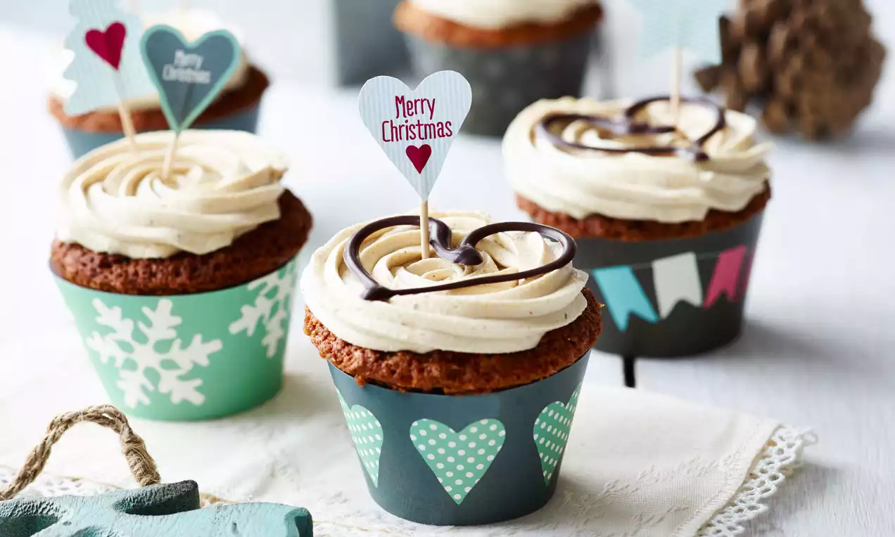 Vanille-Chai-cupcakes met lichtbruine glazuurkrullen en chocoladedecoratie, in kerstvormige groene papieren wikkels op een witte ondergrond