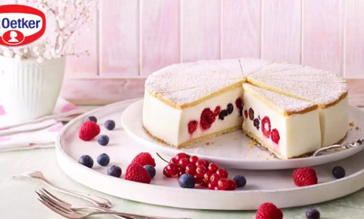 Ronde cheesecake met witte roomkaasvulling doorsneden met rode en blauwe bessen op een licht bord, bestrooid met poedersuiker