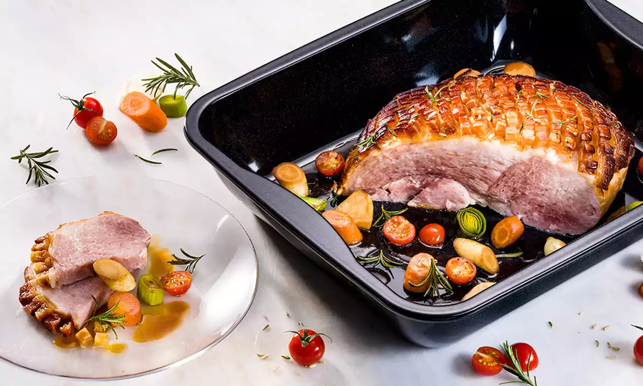 Krustenbraten mit knuspriger goldbrauner Kruste, saftigen Scheiben, glänzender malziger Biersoße und Petersilienzweig auf weißem Teller