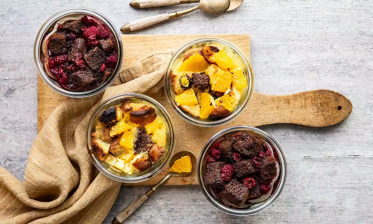 Im Glas geschichteter süßer Gratin mit goldgelber Creme und knusprigen Bröseln, garniert mit fruchtigen Himbeeren und Orangenscheiben
