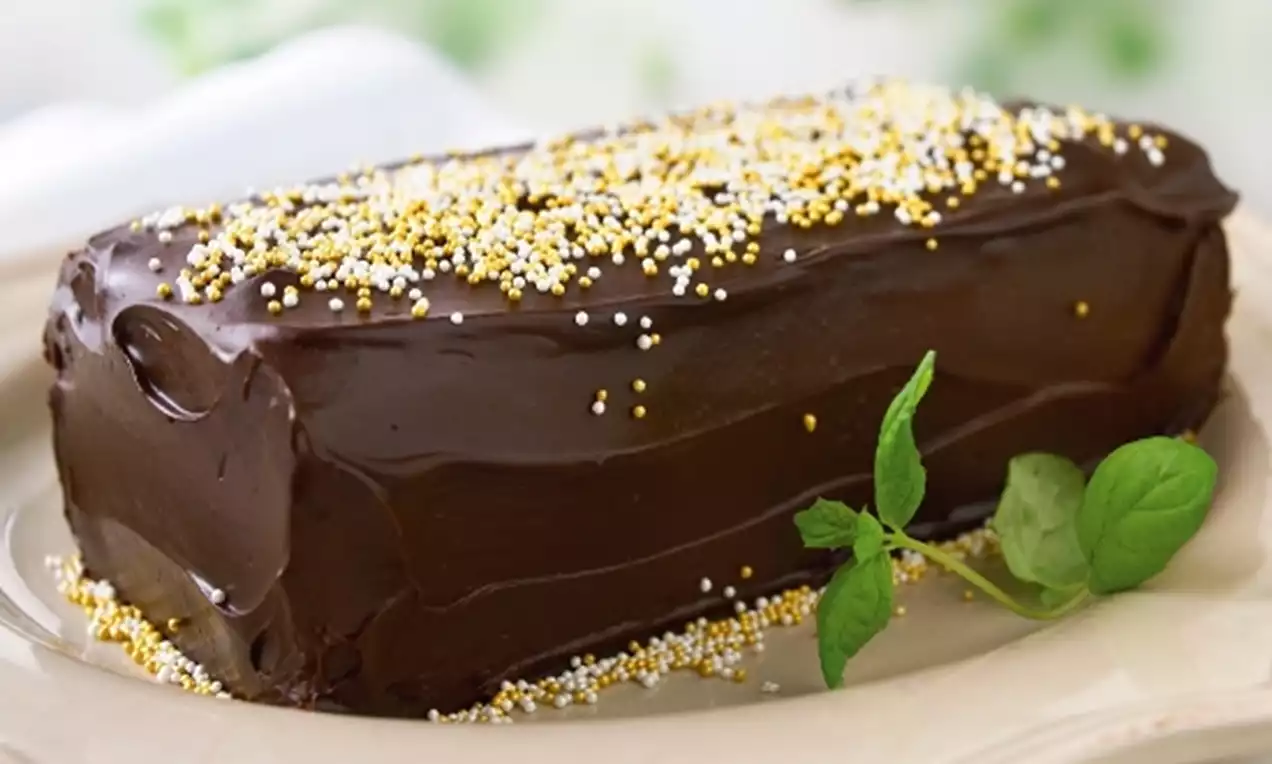 Chokladlängd med blank mörk tryffelglasyr, dekorerad med gulvita strössel, serverad på crèmefärgad tallrik med grön myntakvist