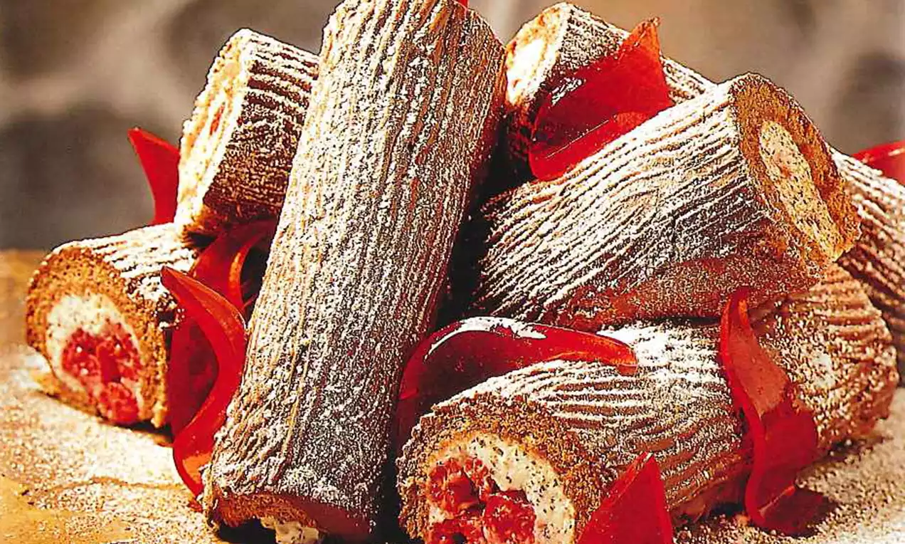 Bruine kerstronkjes met witte crèmevulling en rode accenten, licht bestoven met poedersuiker, gerangschikt op een tafel