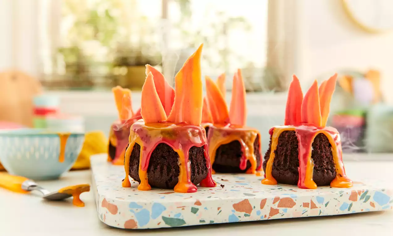 Dark chocolate cupcakes with textured tops, bright red and orange glaze dripping down, crowned with flame-shaped sugar decorations