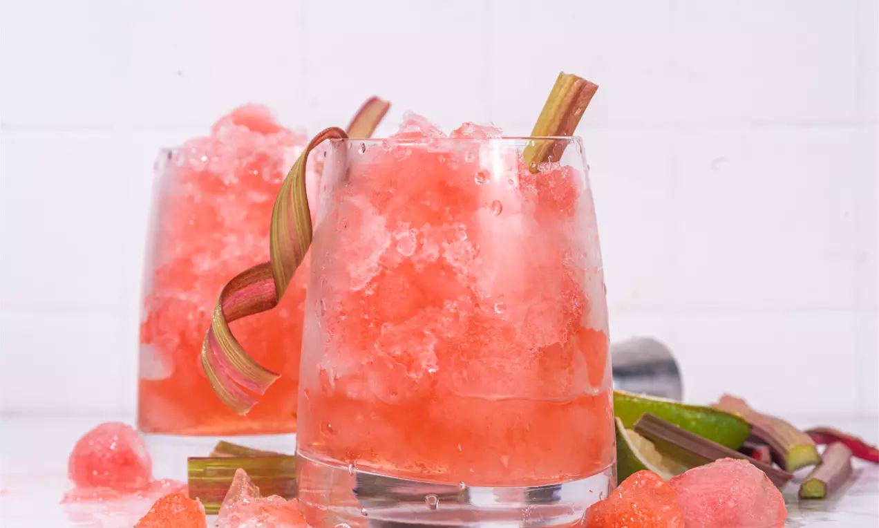 Светло розова гранита с ледени кристали в прозрачна чаша, украсена със зелено-розови стръкове ревен и разпръснати парченца лед