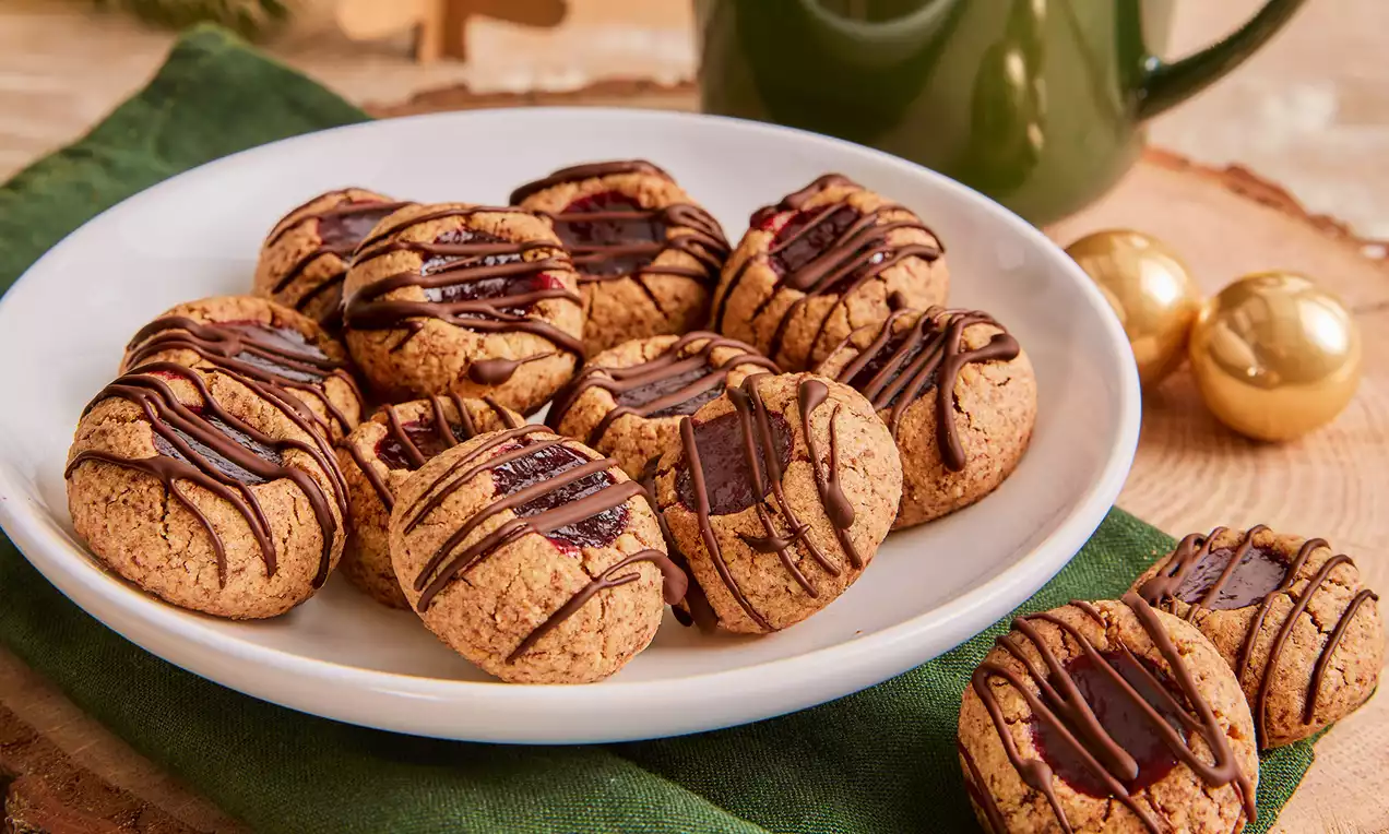 Yuvarlak şekilli, altın kahverengi glutensiz kurabiyeler, ince çikolata şeritleri ve tatlı reçel dolguları ile beyaz bir tabakta sunulmuş