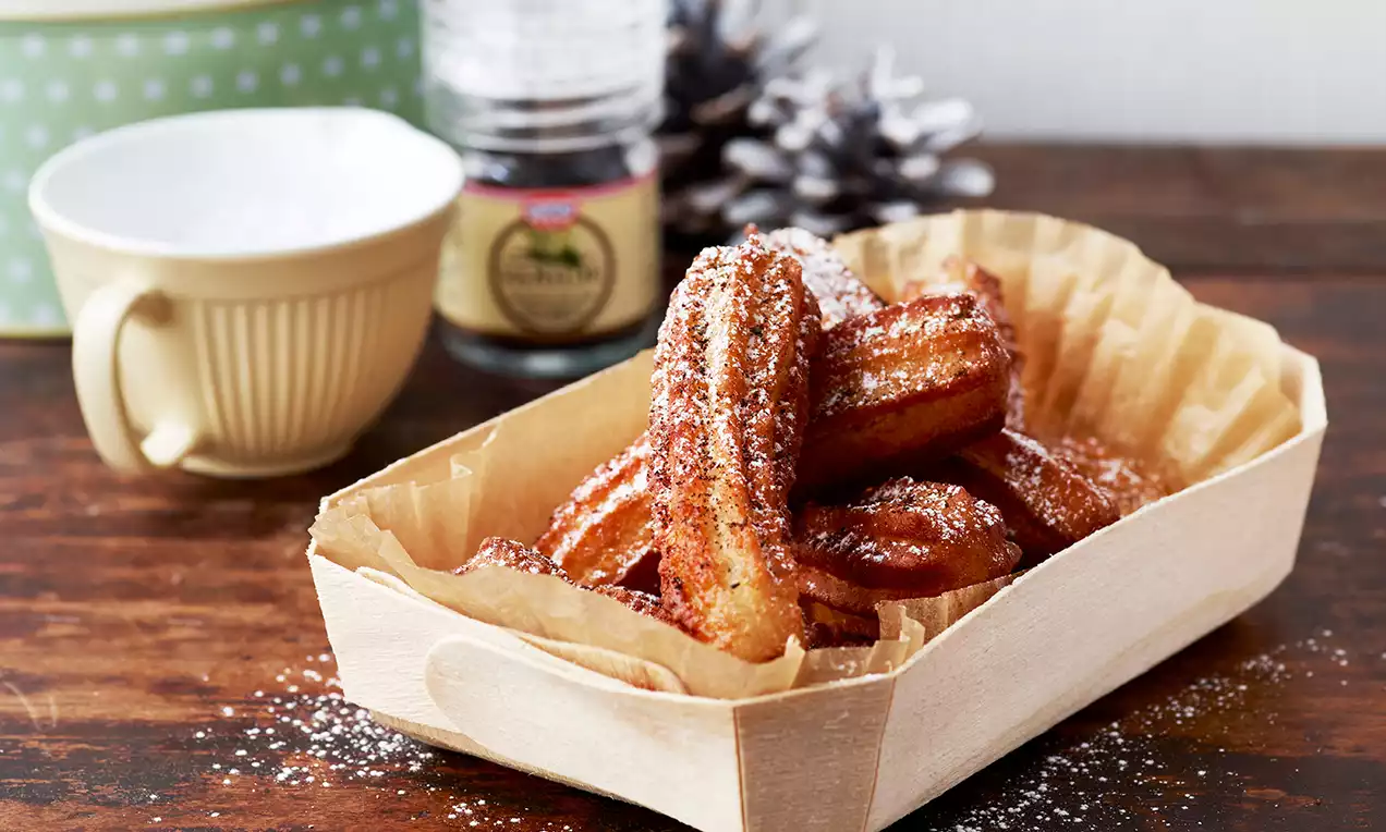 Kullanruskeat, rutisevan rapeat churrot tomusokerilla ripoteltuina, aseteltuina vaaleaan puiseen astiaan voipaperin päälle