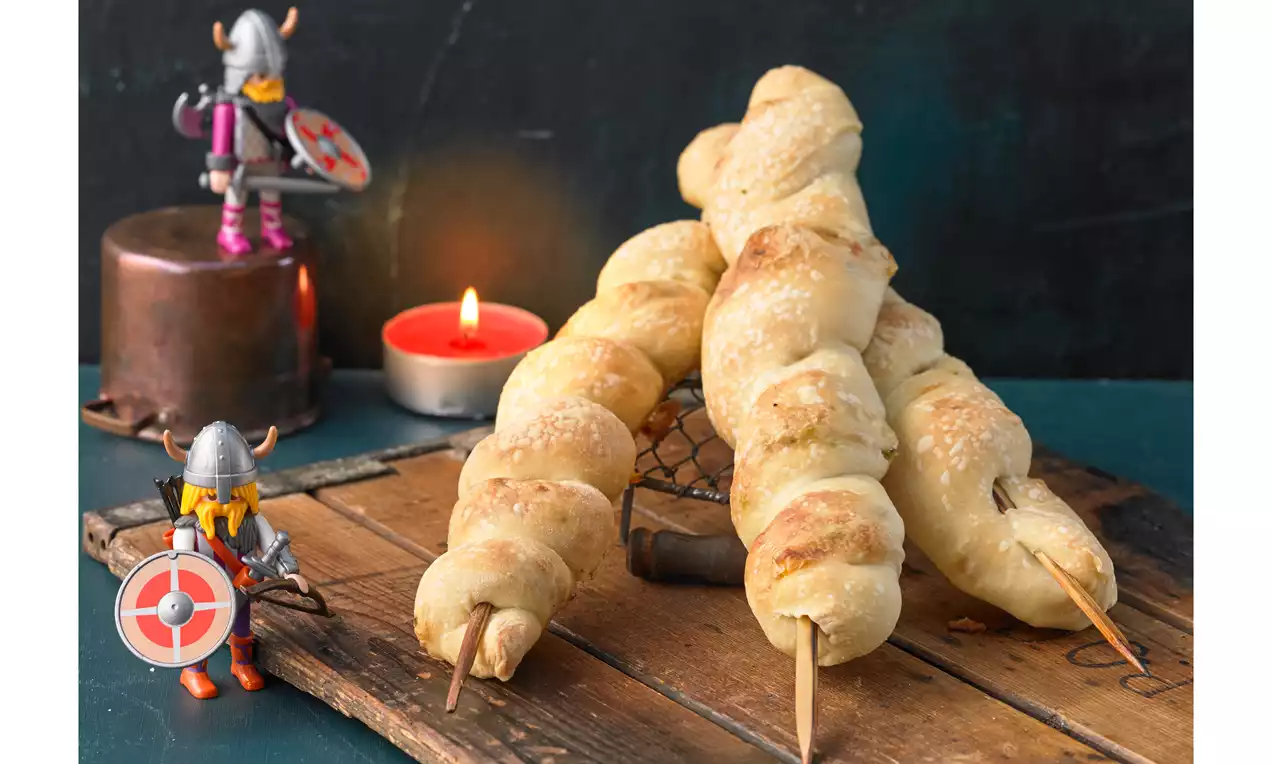Fackelbrot mit goldbrauner Kruste, geschmolzenem Käse und bunter Gemüsefüllung aus Paprika und Zucchini, mit Kräutern auf Holzbrett
