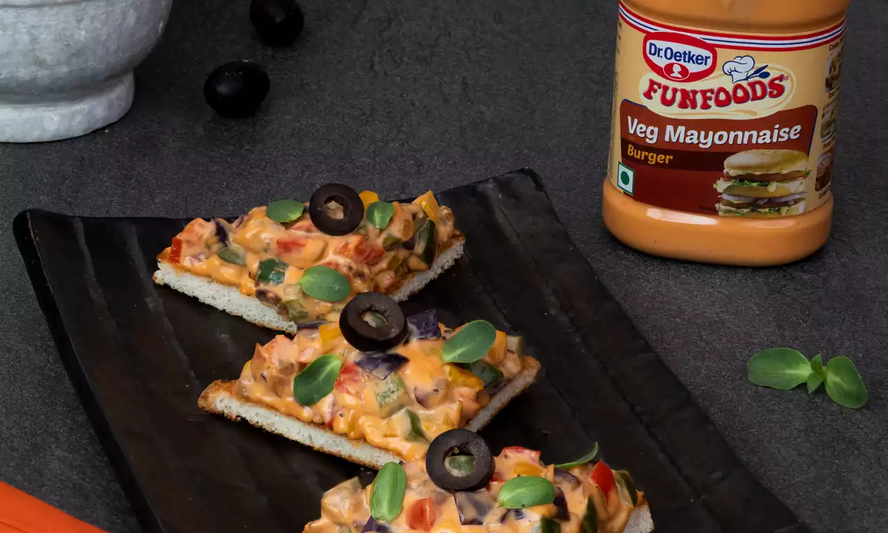 Three rectangular pieces of toasted bread topped with creamy orange spread, diced vegetables, black olive slices, and fresh basil leaves on a black plate