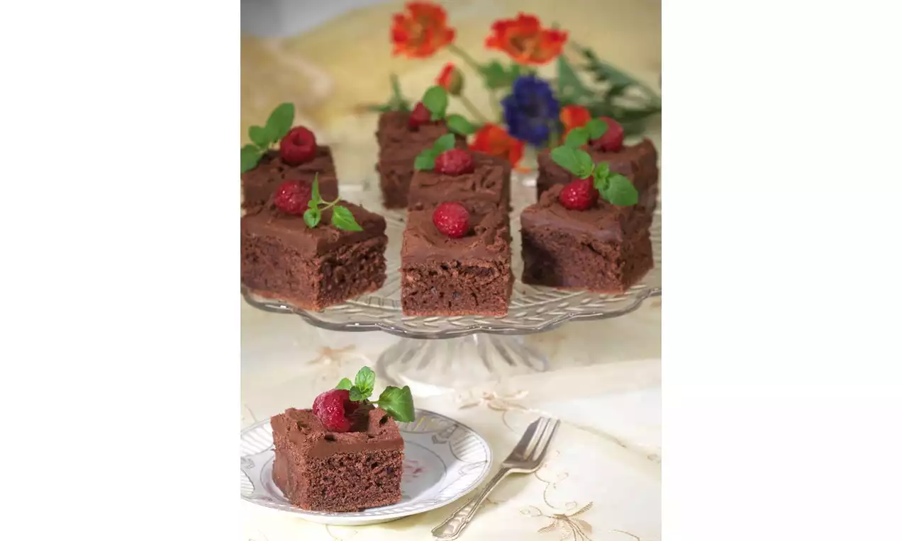 Syvänruskeat browniepalat pehmeällä, hieman murenevalla koostumuksella, jokainen koristeltu vadelmalla ja mintunlehdillä lasisella tarjoiluvadilla