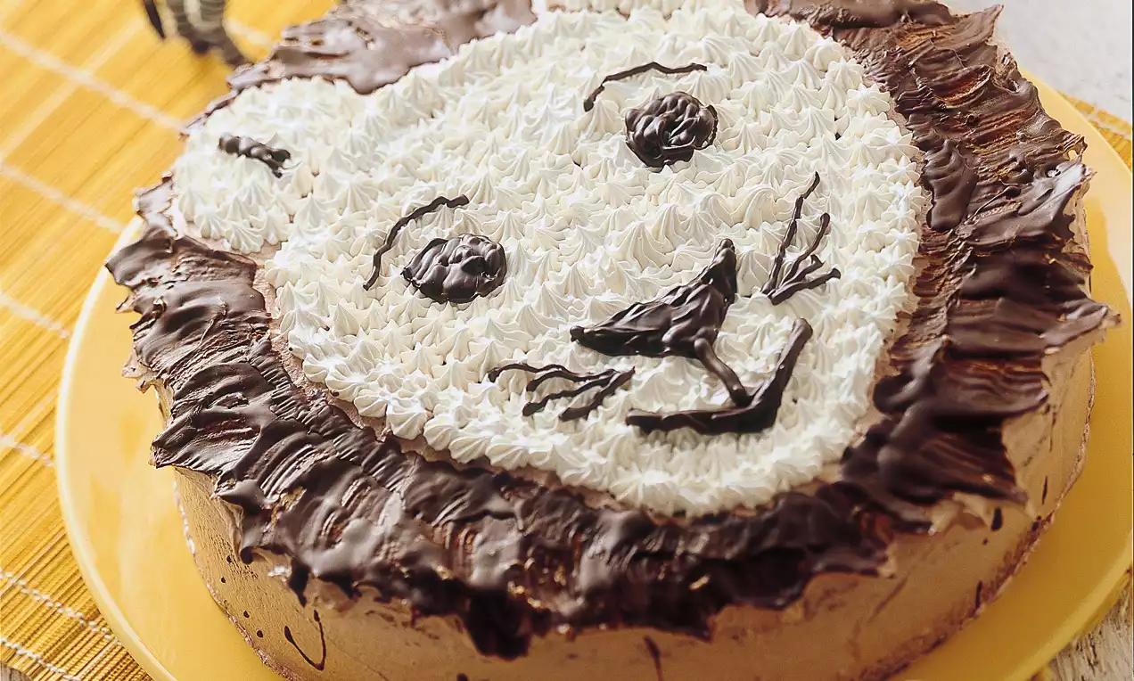 Gâteau rond décoré d'une tête de lion en crème blanche et chocolat, entouré d'une crinière texturée marron sur une assiette jaune