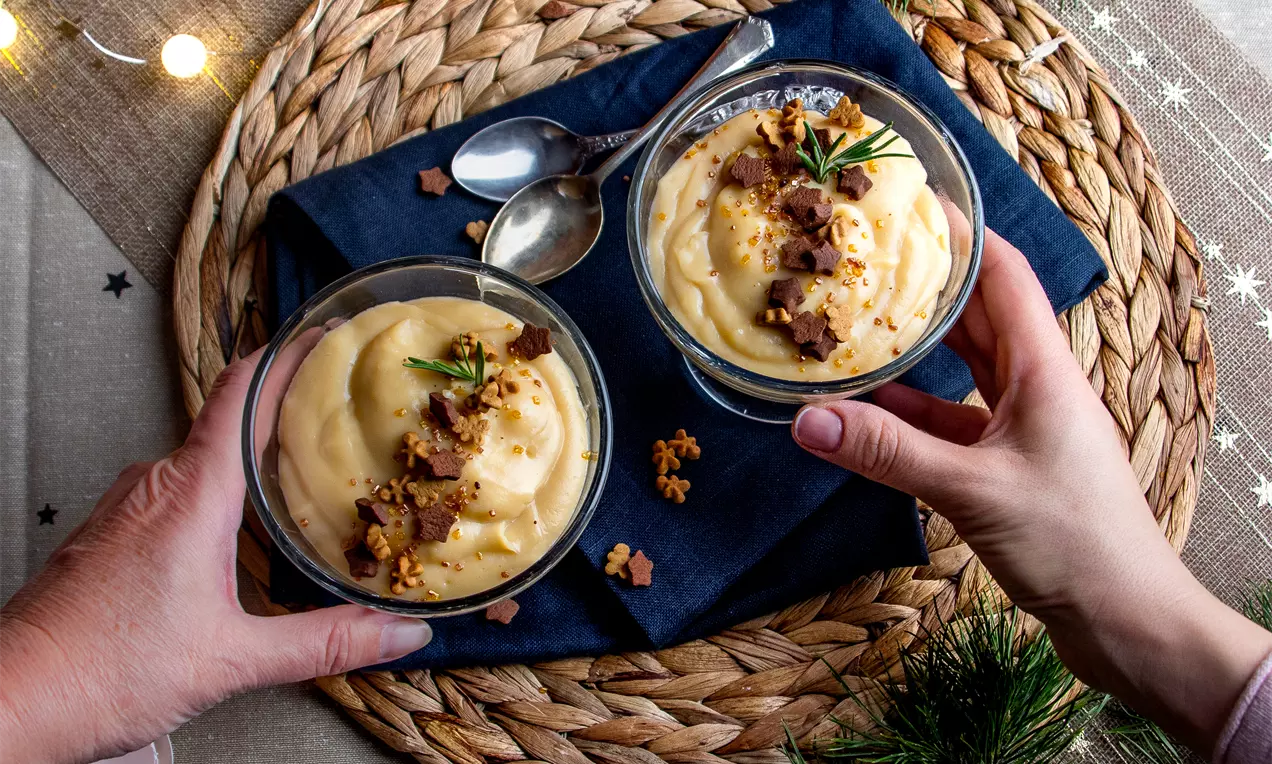 Крем патисери с гладка кремообразна текстура в стъклени купички, украсен с трохи и свежи клонки, поставени върху тъмносиня салфетка