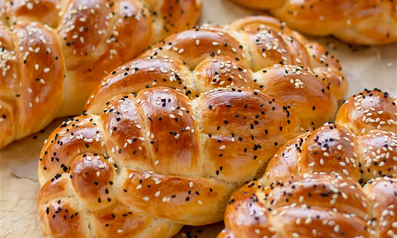 Zlato rjave pletenice z mehko, sijočo skorjo, posute s črnim in belim sezamom, razporejene na pergamentnem papirju