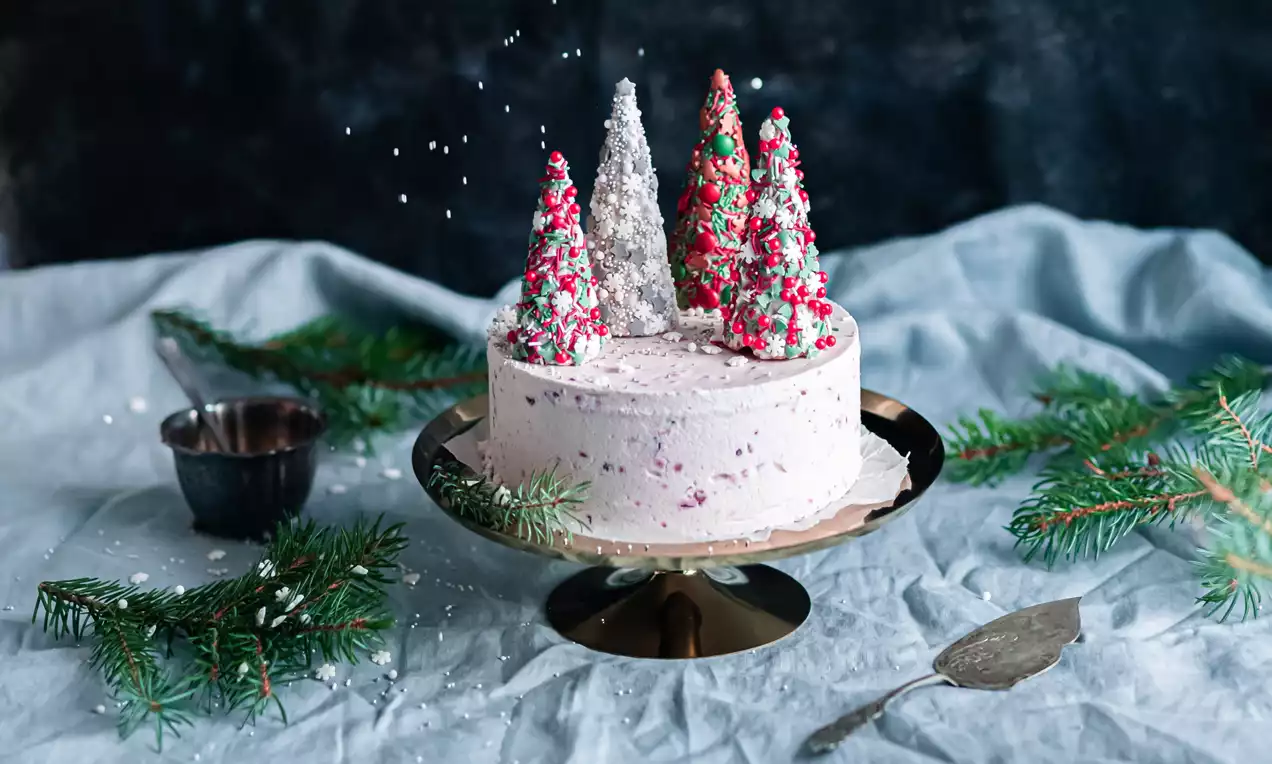 Vaaleanpunainen jäätelökakku, puolukanpilkuilla täyteläinen pinta, koristeltu värikkäillä suklaakuusilla metallivadin keskellä