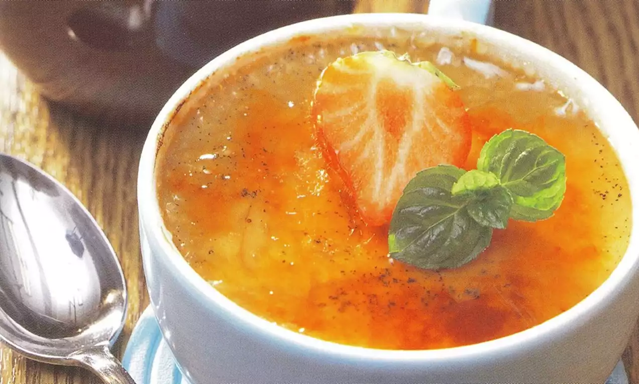 Crème dorée à la surface caramélisée, garnie d’une moitié de fraise rouge vif et de feuilles de menthe sur un fond bois clair