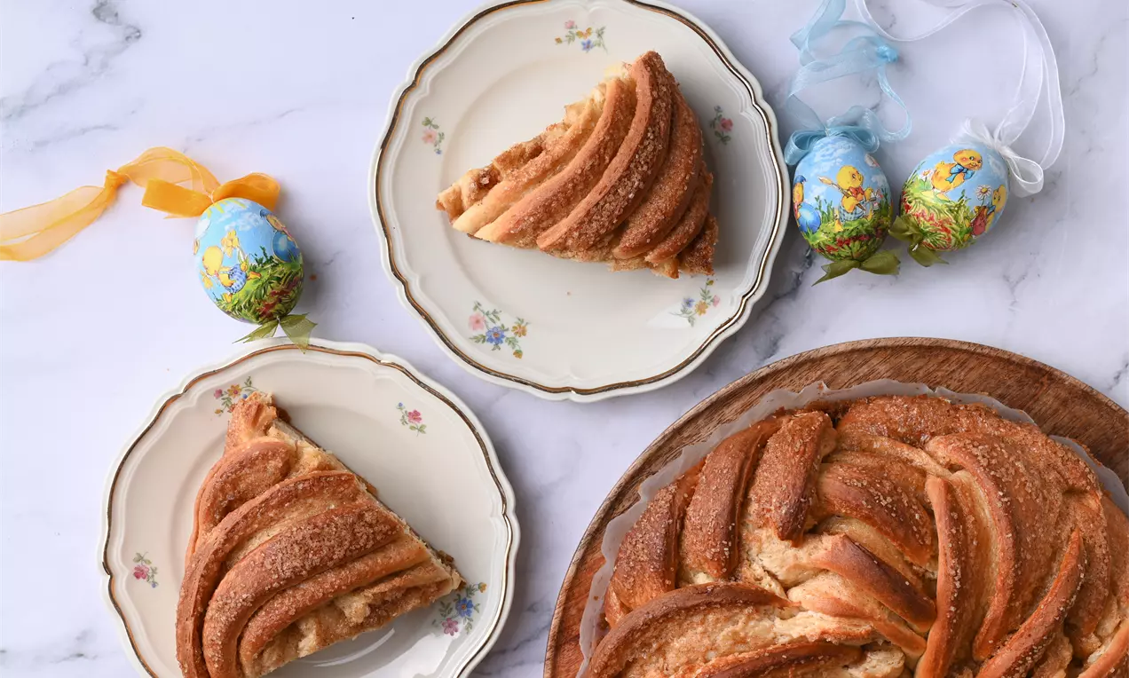 Козуначено венче с наситено златиста кора и ронлива текстура, украсено с извити слоеве върху дървена плоча и порцеланови чинии